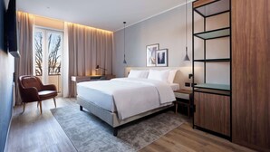 A modern bedroom with a large bed, a wooden wardrobe, a desk, and a chair. - Radisson Hotel Ferrara (Ferrara)