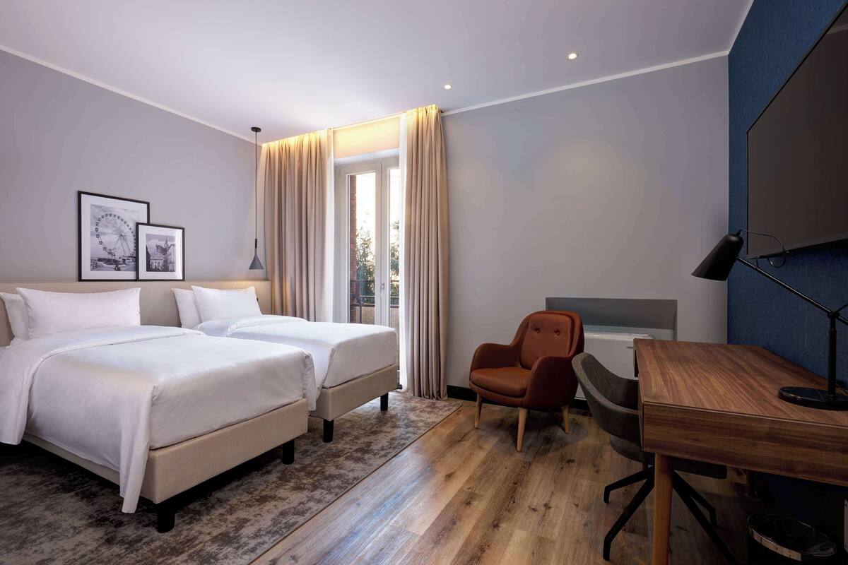 Ein Hotelzimmer mit zwei Betten, einem Schreibtisch, einem Stuhl und einem Fernseher.