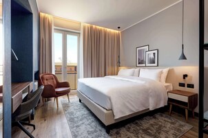 Habitación de hotel moderna con una cama grande, un escritorio, una silla y vistas al exterior.