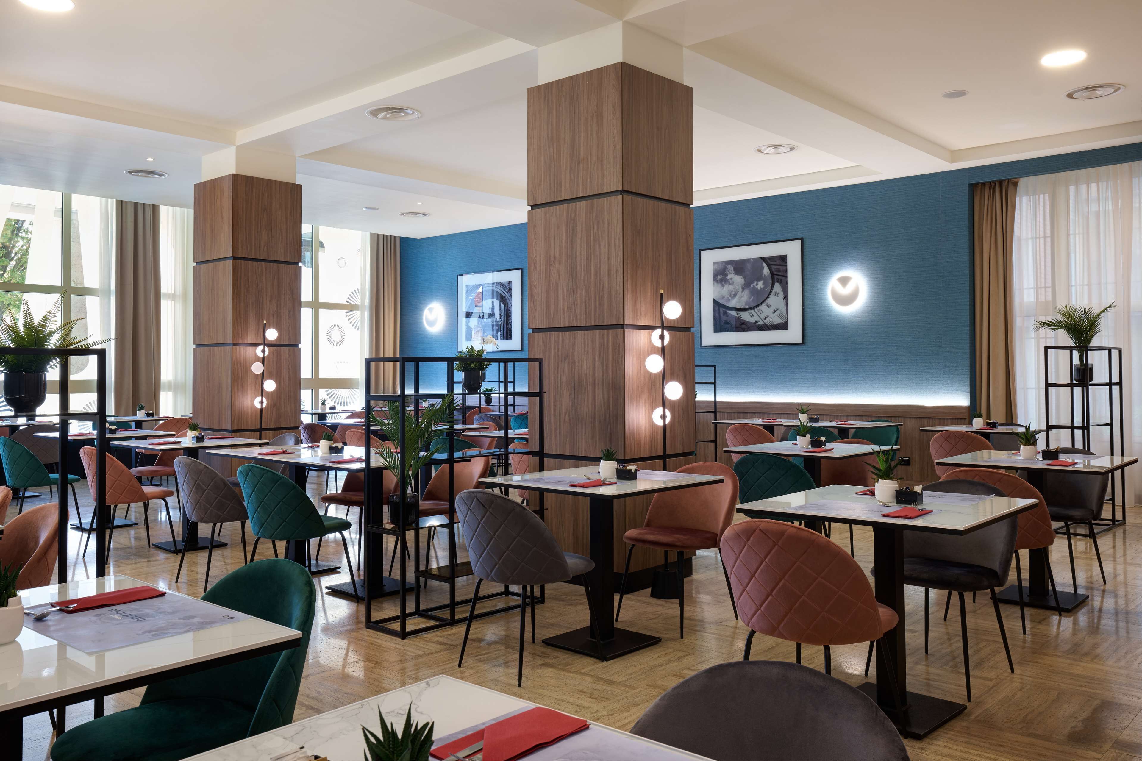 A modern dining area with multiple tables and chairs, wooden pillars, and framed artwork on the walls.