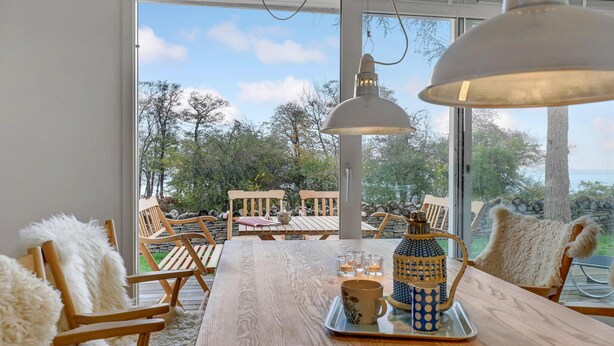 A dining area with a wooden table, chairs, and a view of the outdoors. - 3 bedroom beautiful home in Gudhjem (Gudhjem)