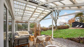 A covered patio with a glass enclosure, outdoor seating, and a view of the surrounding garden and trees. - 3 bedroom beautiful home in Gudhjem (Gudhjem)