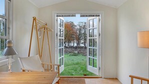 A room with a large open door leading to a grassy area, a wooden chair, a table, and a lamp. - 3 bedroom beautiful home in Gudhjem (Gudhjem)