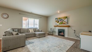 A living room with a sectional sofa, a fireplace, a flat-screen TV, and a large window with blinds. - Bonney Lake House INN  W/Jacuzzi and Centralized AC (Bonney Lake)
