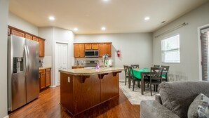 A modern kitchen with a central island, wooden cabinets, stainless steel appliances, and a dining area with a green table and chairs. - Bonney Lake House INN  W/Jacuzzi and Centralized AC (Bonney Lake)