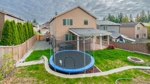 A residential backyard with a trampoline, a covered patio, and a stone fire pit. - Bonney Lake House INN  W/Jacuzzi and Centralized AC (Bonney Lake)