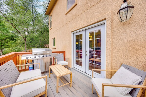 En udendørs terrasse med grill, siddepladser og en skydedør.