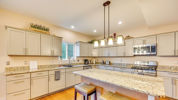 A kitchen with white cabinets, granite countertops, a large island with stools, a stainless steel microwave, and a gas stove. - 2 Mi to Dtwn Colorado Springs: Home w/ Large Yard! (Colorado Springs)