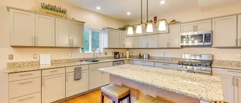 A kitchen with white cabinets, granite countertops, a large island with stools, a stainless steel microwave, and a gas stove.