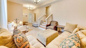 A spacious living room with a large beige sofa, a patterned armchair, and a wooden coffee table. A staircase leads to an upper level, and a chandelier hangs from the ceiling. - 2 Mi to Dtwn Colorado Springs: Home w/ Large Yard! (Colorado Springs)