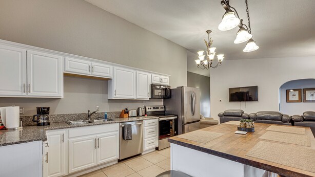 A modern kitchen with white cabinets, stainless steel appliances, a coffee maker, and a dining area with a wooden table and chairs. - Family-Friendly Home 2 Mi to Dtwn Colorado Springs (Colorado Springs)