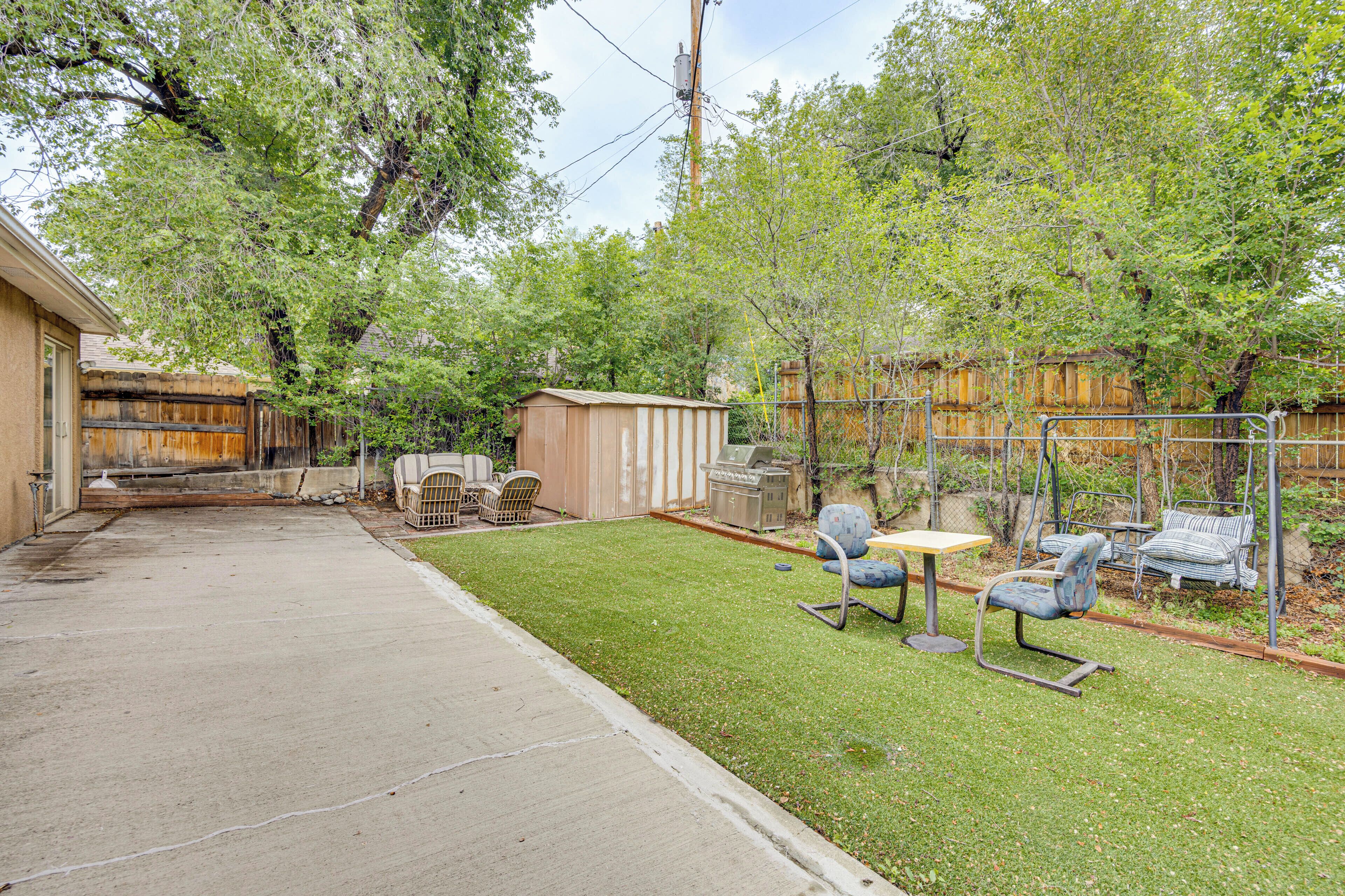 A backyard with a lawn, a wooden shed, a grill, and outdoor furniture.