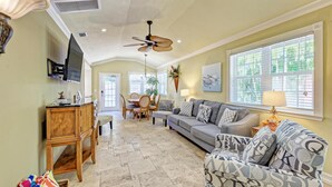 A spacious living room with a grey sofa, a wooden cabinet, and a dining area with a table and chairs. - Anna Maria Island Surfside Bungalow (Holmes Beach)