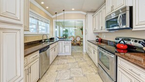 A kitchen with white cabinetry, a central island, stainless steel appliances, and a dining area in the background. - Anna Maria Island Surfside Bungalow (Holmes Beach)