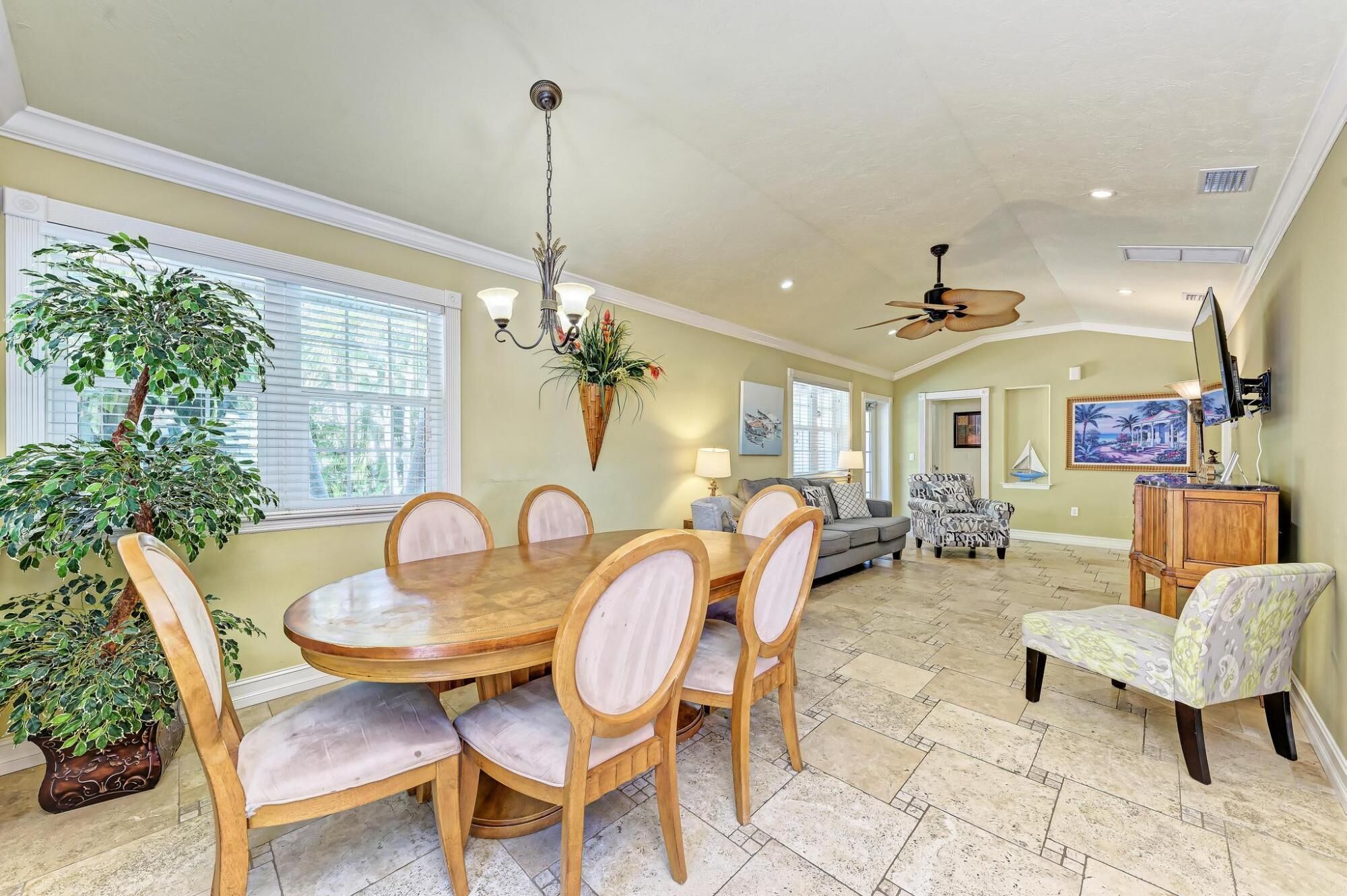 A dining area with a round wooden table and six chairs, a chandelier, and a large potted plant.