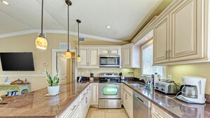 A kitchen with a large island, stainless steel appliances, and pendant lighting.
