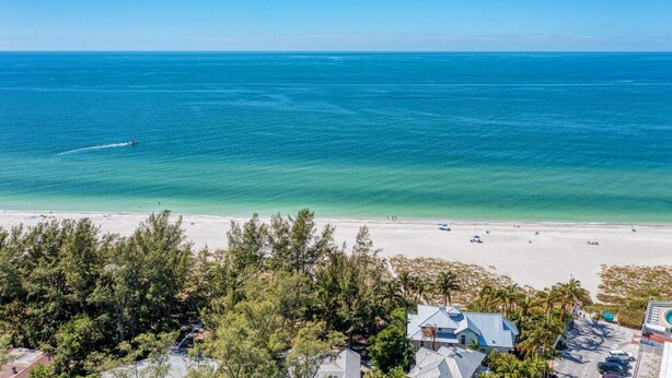 A beach view with clear skies, a boat on the water, and a few people on the sand.