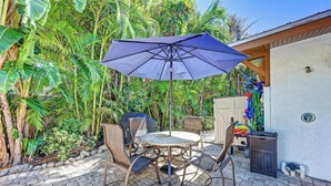 An outdoor patio with a round table and four chairs, a blue umbrella, and a grill.
