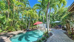 A swimming pool surrounded by palm trees and a patio area with outdoor furniture.