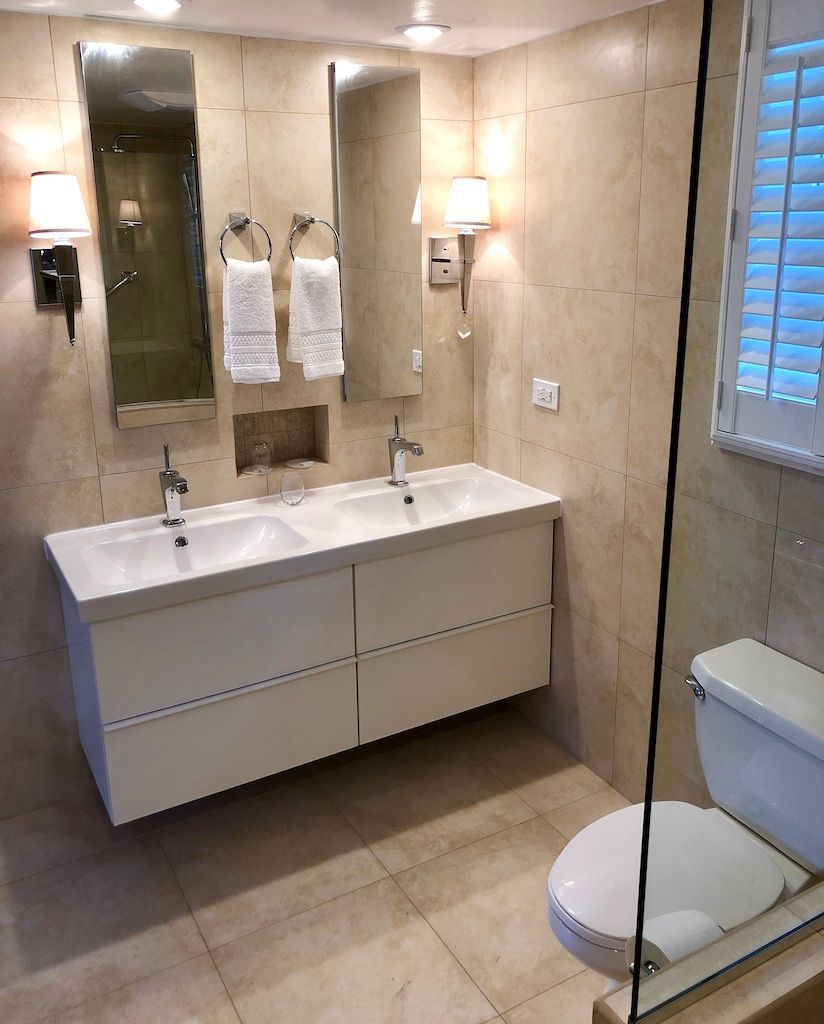 Et moderne badeværelse med et dobbelt håndvaskebord, toilet og en glasbrusekabine.