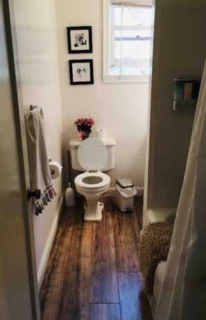 A small bathroom with a toilet, a trash can, and a window.