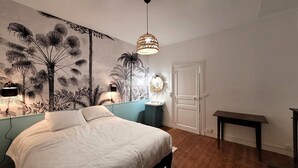 Un dormitorio con cama, un mural en la pared, una lámpara colgante, una mesita de noche y una puerta.
