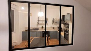 Una cocina moderna con un amplio ventanal, electrodomésticos integrados y un comedor visible a través de la ventana.