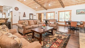 Ein geräumiges Wohnzimmer mit Holzboden, einer großen Couch, einem Couchtisch und einem Essbereich mit Stühlen und Tisch.