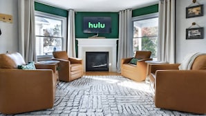 Un salon doté d’une cheminée, de fauteuils en cuir, d’un grand tapis et d’un téléviseur fixé au-dessus de la cheminée, sur lequel est diffusée la plateforme « Hulu ».