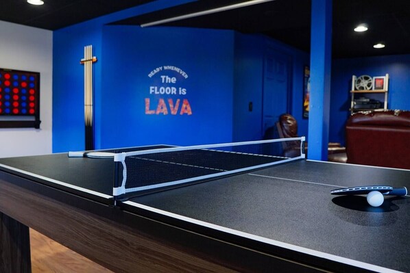 Uma mesa de ping pong em um quarto com paredes azuis e um letreiro que diz 'O chão está em lava'.