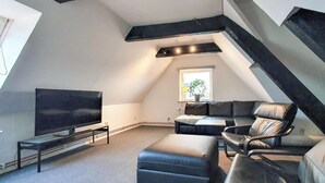 Een moderne woonkamer in loftstijl, met een grote flatscreentelevisie, een zwarte leren bank en een bijzettafeltje.