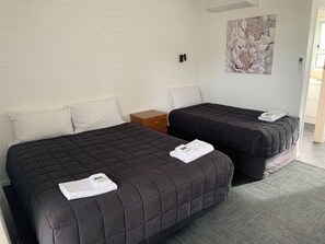 A hotel room with two beds, a nightstand, a wall-mounted thermostat, and a painting. - Brooklyne Motel Sanson (Sanson)