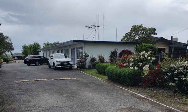 Un aparcamiento con dos coches, un edificio con antena parabólica y macizos de flores bien cuidados.