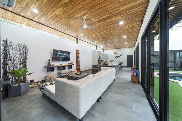 A modern living room with a large sofa, a flat-screen TV, and a wooden ceiling.