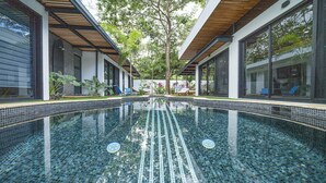 Une piscine intérieure moderne, dotée d’une eau cristalline, entourée d’un patio couvert agrémenté de sièges et de plantes.