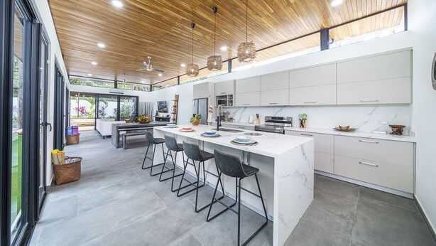 Une cuisine moderne dotée d’un grand îlot central, de tabourets de bar et offrant une vue sur l’extérieur.