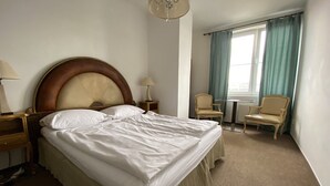 Et hotelværelse med en stor seng, to sengeborde, en stol, et lille bord og et vindue med gardiner.