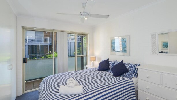 Ein Schlafzimmer mit einem großen Bett, einem Deckenventilator, einer Glastür zu einem Außenbereich und einer weißen Kommode.