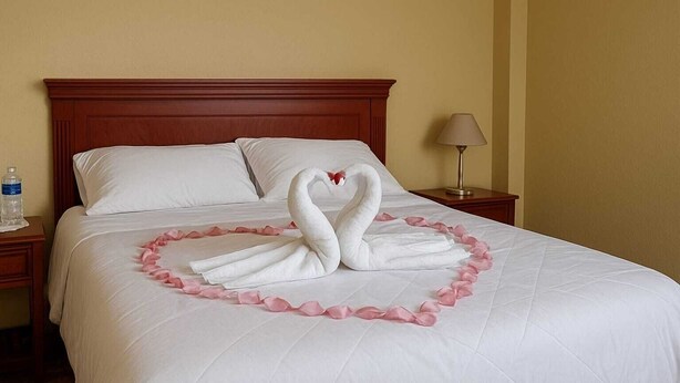 A neatly made bed with a swan and heart-shaped decoration made of rose petals. - Hostería Cotopaxi Tour (Tanicuchi)