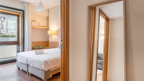 A modern hotel room with a large bed, a bedside table, a lamp, and a view of the city through a window. - GuestReady - Cozy Bright apartment with a Balcony (Porto)
