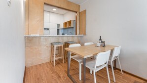 A compact dining area with a wooden table and white chairs, a small kitchen with white cabinets, and a wooden counter. - GuestReady - Cozy Bright apartment with a Balcony (Porto)