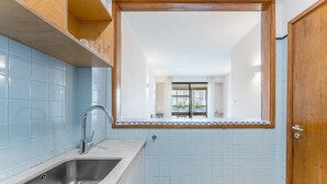 A compact kitchen with a sink, a wooden door, and a view into a dining area. - GuestReady - Cozy Bright apartment with a Balcony (Porto)
