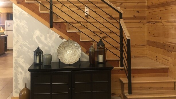 A wooden staircase with a metal railing, a black console table with decorative items, and a wooden wall with a carved design. - Powerhouse Cabin Black River falls Wisconsin  (Black River Falls)
