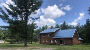 A wooden cabin with a metal roof, surrounded by a grassy field and trees. - Powerhouse Cabin Black River falls Wisconsin  (Black River Falls)