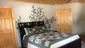 A bedroom with a bed, wooden doors, a wall with a leaf pattern, and a lamp. - Powerhouse Cabin Black River falls Wisconsin  (Black River Falls)