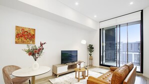 A modern living room with a sofa, a TV, a dining table, and a large window. - Experience serenity in this modern haven
Train/Ferry to City~Shops~Parking (Ryde)