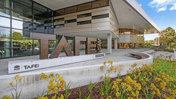 A modern building with large letters spelling "TAFE" on the facade, a landscaped area with yellow flowers, and a clear sky. - Experience serenity in this modern haven
Train/Ferry to City~Shops~Parking (Ryde)