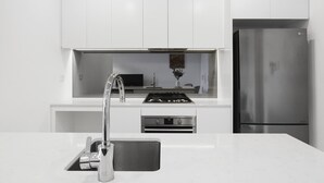 A modern kitchen with white cabinetry, stainless steel appliances, and a built-in oven. - Experience serenity in this modern haven
Train/Ferry to City~Shops~Parking (Ryde)