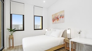 A modern bedroom with a large bed, bedside tables, a desk, and a potted plant. - Experience serenity in this modern haven
Train/Ferry to City~Shops~Parking (Ryde)