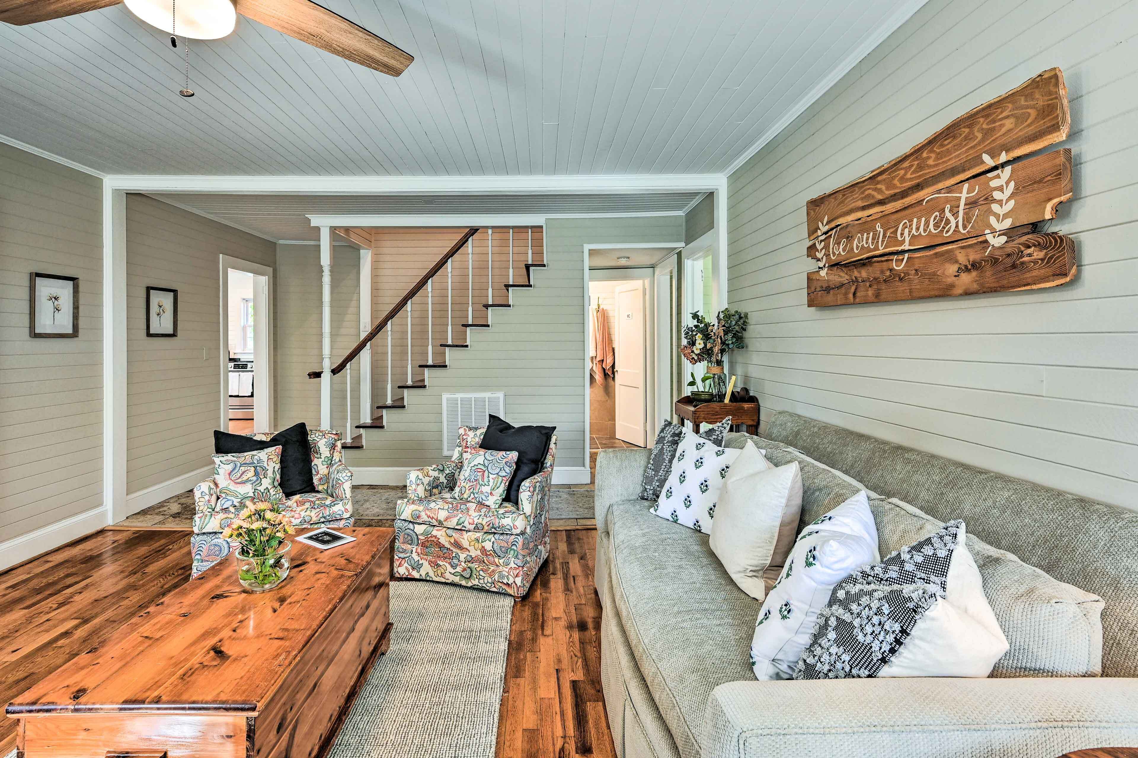 A spacious living room with a wooden coffee table, patterned armchairs, a grey sofa, and a staircase leading to another level.